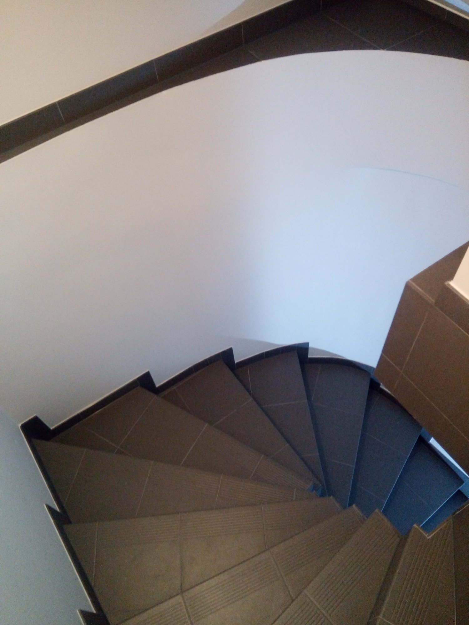 Spiralne schody wyłożone brązowymi płytkami ceramicznymi, widok z góry, z ciemnobrązowym wykończeniem sufitu.