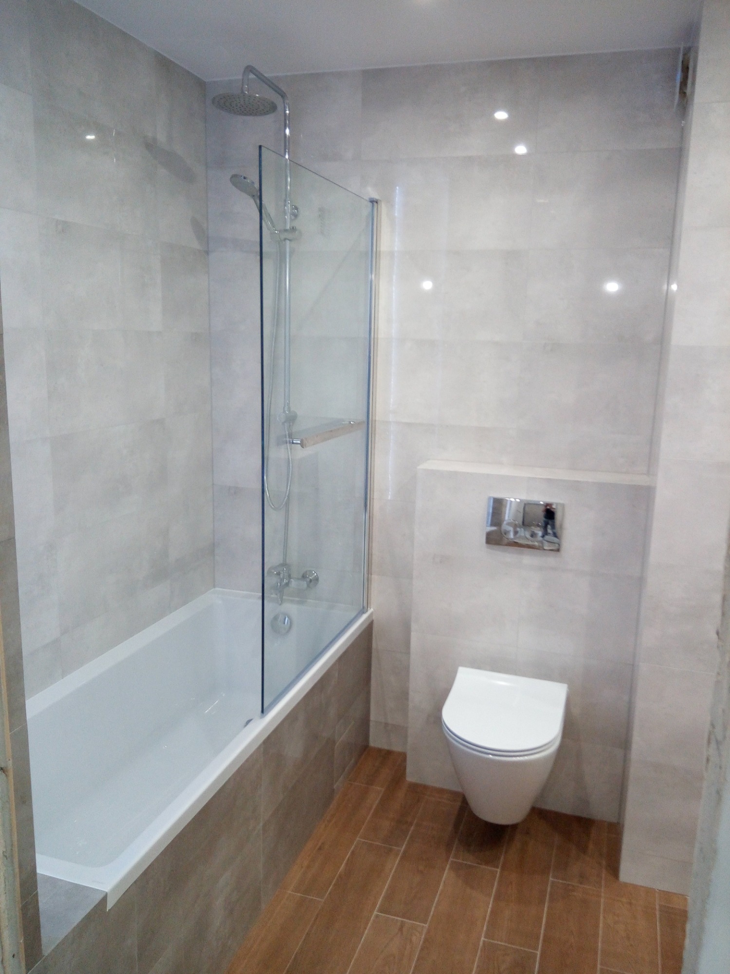 Wykończona łazienka we Wrocławiu z wanną z parawanem szklanym, toaletą podwieszaną i płytkami imitującymi kamień na ścianach oraz drewnopodobną podłogą.