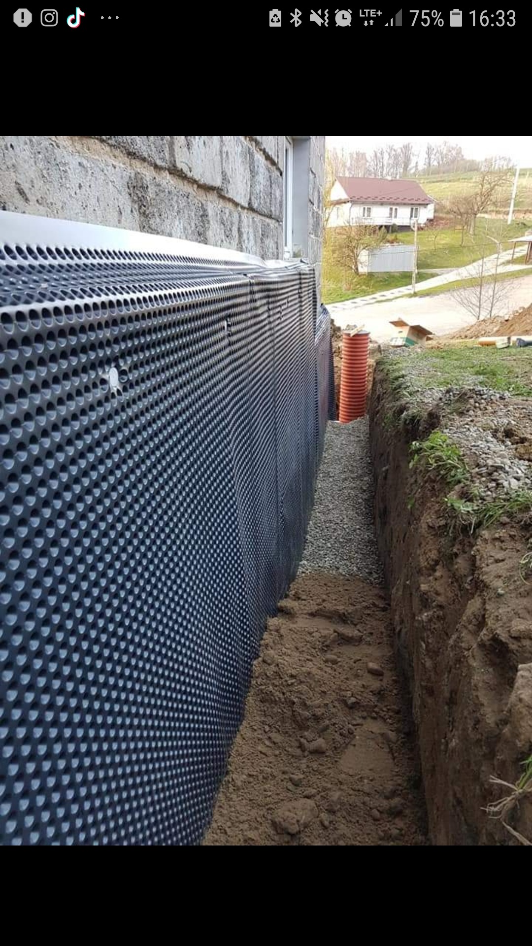 Izolacja fundamentów budynku z użyciem folii kubełkowej, widoczny wykop z drenażem żwirowym i rurą drenarską.