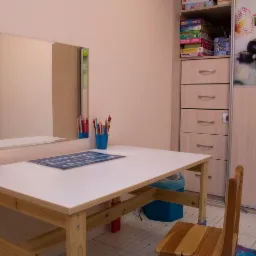 Gabinet terapeutyczny z biurkiem, krzesłem i lustrem, na biurku kolorowe kredki i plansza edukacyjna, w tle szafa z grami i dekoracją zen.