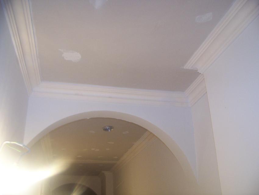 Wnętrze z łukowym przejściem i listwami dekoracyjnymi przy suficie, na którym widoczne są ślady po szpachlowaniu.