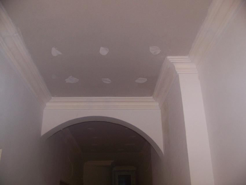 Wnętrze w trakcie wykańczania z widoczną zabudową z płyt kartonowo-gipsowych, sztukaterią gipsową i łukowym przejściem, na suficie widoczne miejsca po szpachlowaniu.