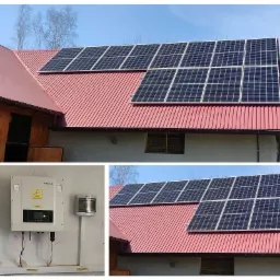 Panel słoneczny na czerwonym, blaszanym dachu budynku z widocznym falownikiem SOFAR i skrzynkami zabezpieczeń AC/DC na ścianie.