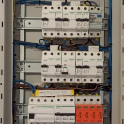 Rozdzielnica elektryczna z bezpiecznikami i przewodami w skrzynce, zamontowana w Warszawie, widoczne elementy marki Schneider i Simtec.