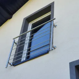 Nowoczesna balustrada balkonowa ze stali nierdzewnej z poziomymi prętami, zamontowana na elewacji budynku z oknem w szarej ramie.