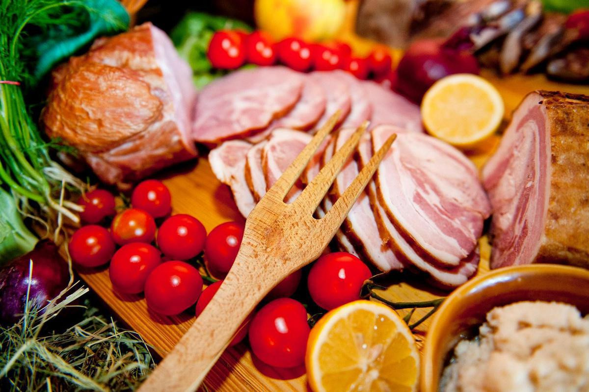 Kompozycja wędlin, pomidorków cherry, cytryny i zieleniny na drewnianej desce z rustykalną, drewnianą łyżką z trzema zębami na pierwszym planie.