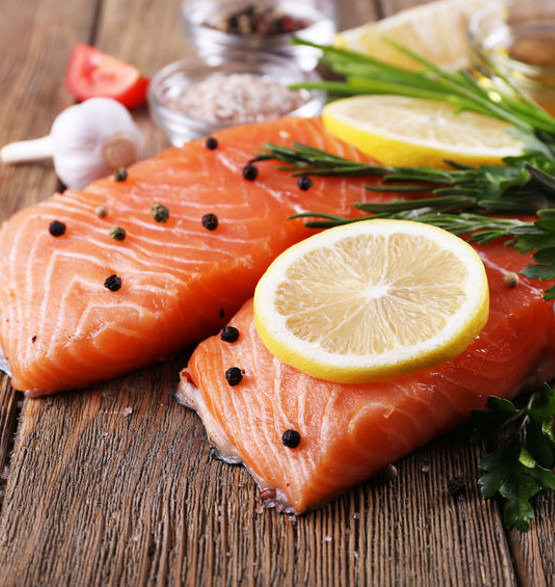 Dwa filety z łososia z plasterkami cytryny, czarnym pieprzem i ziołami na rustykalnym drewnianym stole, przygotowane do cateringu w Gdańsku.