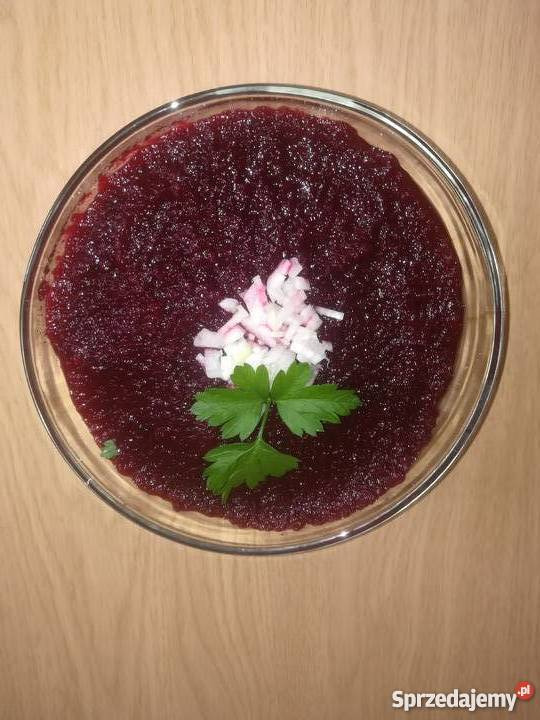 Sałatka buraczkowa w szklanej misce, udekorowana posiekaną cebulą i listkiem zielonej pietruszki, ustawiona na drewnianym blacie.