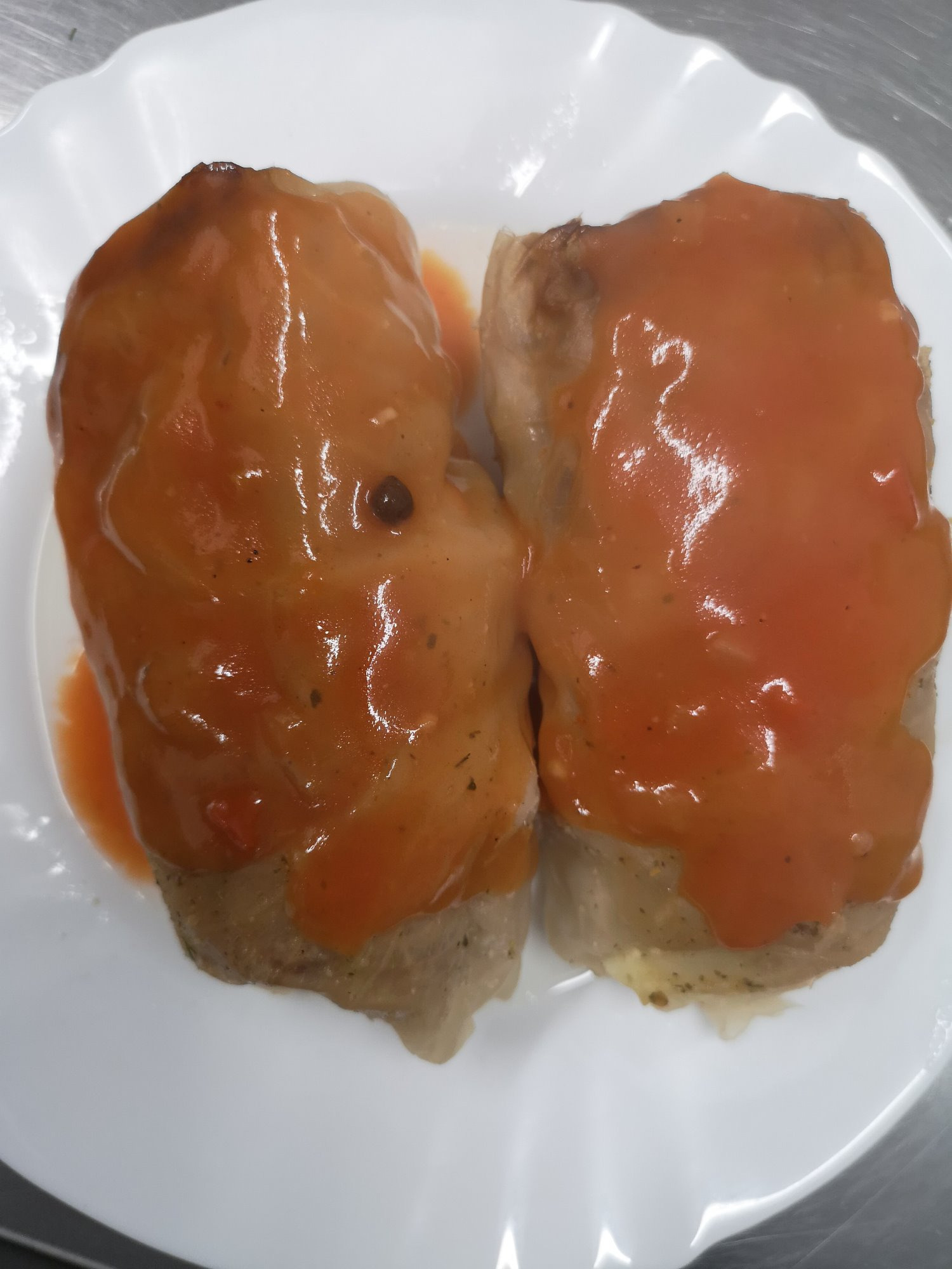 Dwa gołąbki polane pomidorowym sosem na białym talerzu, widoczne przyprawy i farsz.