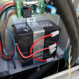 Wnętrze skrzynki sterowniczej z akumulatorami FIAMM FG201, bezpiecznikiem, kondensatorami i okablowaniem.