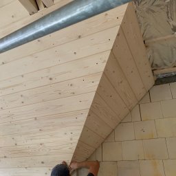 FIRMA USŁUGOWO-REMONTOWA - Montaż drewnianej boazerii na poddaszu, widoczne deski układane poziomo, izolacja pokryta folią aluminiową oraz fragment ściany z bloczków.