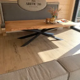 Stół z blatem z litego drewna i metalową podstawą w kształcie gwiazdy, ustawiony w drewnianym domu, dekoracje na stole, widoczny fragment sofy.