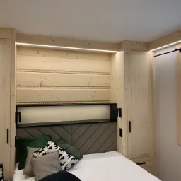 Drewniana zabudowa sypialni z szafami po bokach łóżka, oświetleniem LED i panelami ściennymi z motywem liny.
