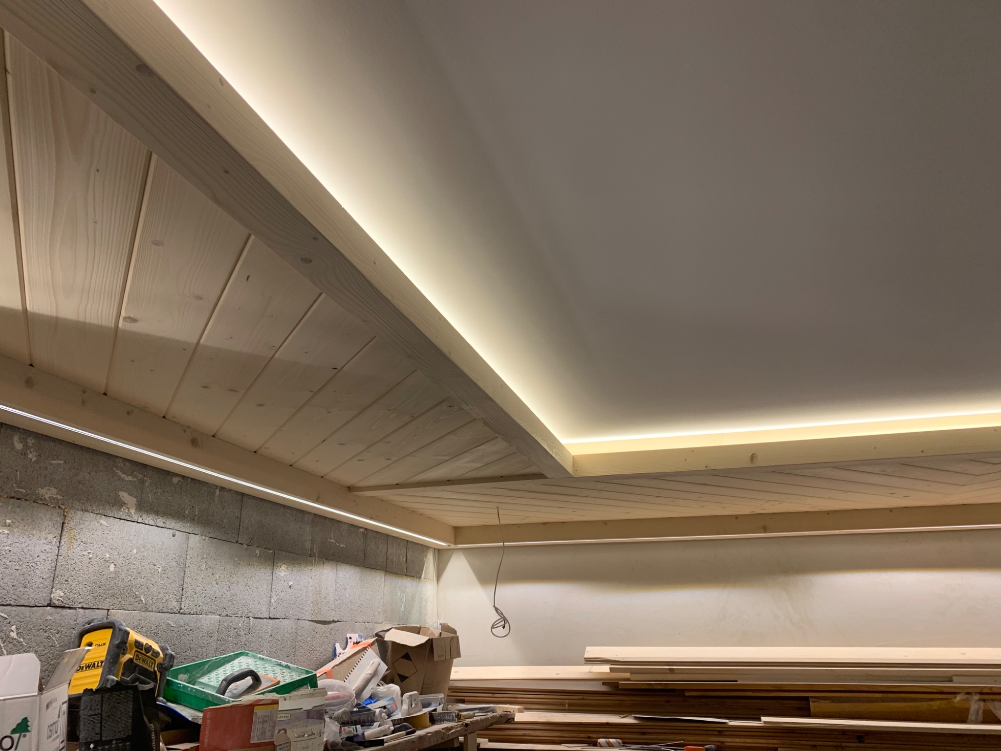 Drewniany sufit podwieszany z oświetleniem LED w trakcie montażu, widoczne narzędzia i materiały budowlane w tle.