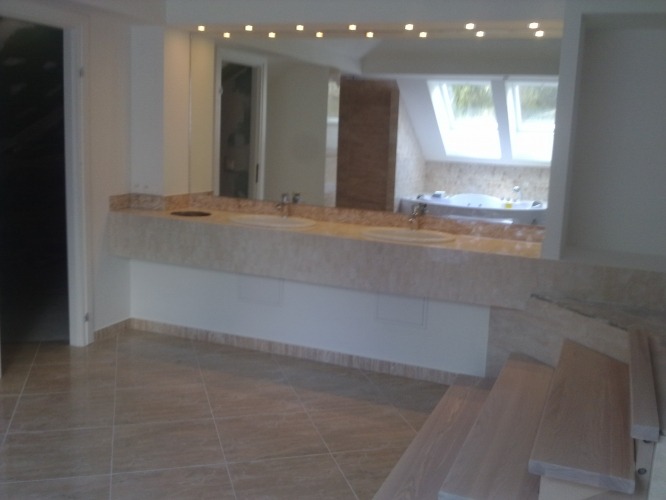 Nowoczesna łazienka z marmurowym blatem, podwójną umywalką i oświetleniem punktowym, widok na wannę w tle