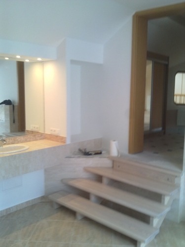 Jasna łazienka w trakcie prac wykończeniowych: widoczne schodki prowadzące do wyższej części pomieszczenia, umywalka z marmurowym blatem, narzędzia i rolka papieru na blacie, świeżo pomalowane ściany.