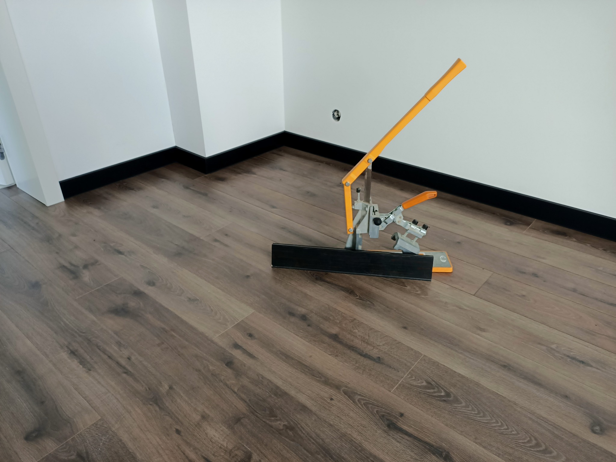 Nowo ułożona, brązowa podłoga w Krakowie z narzędziem do cięcia paneli podłogowych, widoczne czarne listwy przypodłogowe.