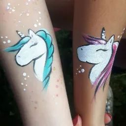 Dwa ramiona z namalowanymi jednorożcami: jeden z turkusową grzywą, drugi z różową, oba w stylu dziecięcym z białymi kropkami dookoła.