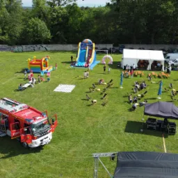 Widok z góry na piknik firmowy na trawie z dmuchańcami, trampolinami, namiotem cateringowym i wozem strażackim