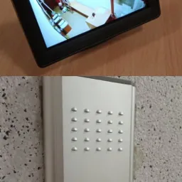 Monitor wideodomofonu wyświetlający obraz z kamery zainstalowanej wewnątrz budynku, obok zamontowany panel zewnętrzny wideodomofonu firmy Orno z podświetlanym przyciskiem.