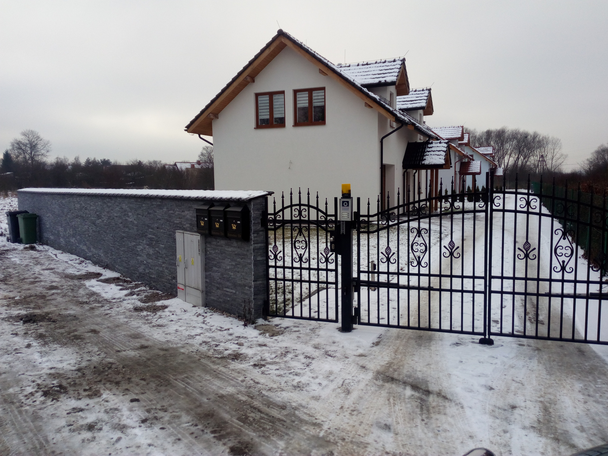 Nowe domy jednorodzinne w zabudowie szeregowej w Krakowie, z kutą bramą wjazdową i murowanym ogrodzeniem w zimowej scenerii.