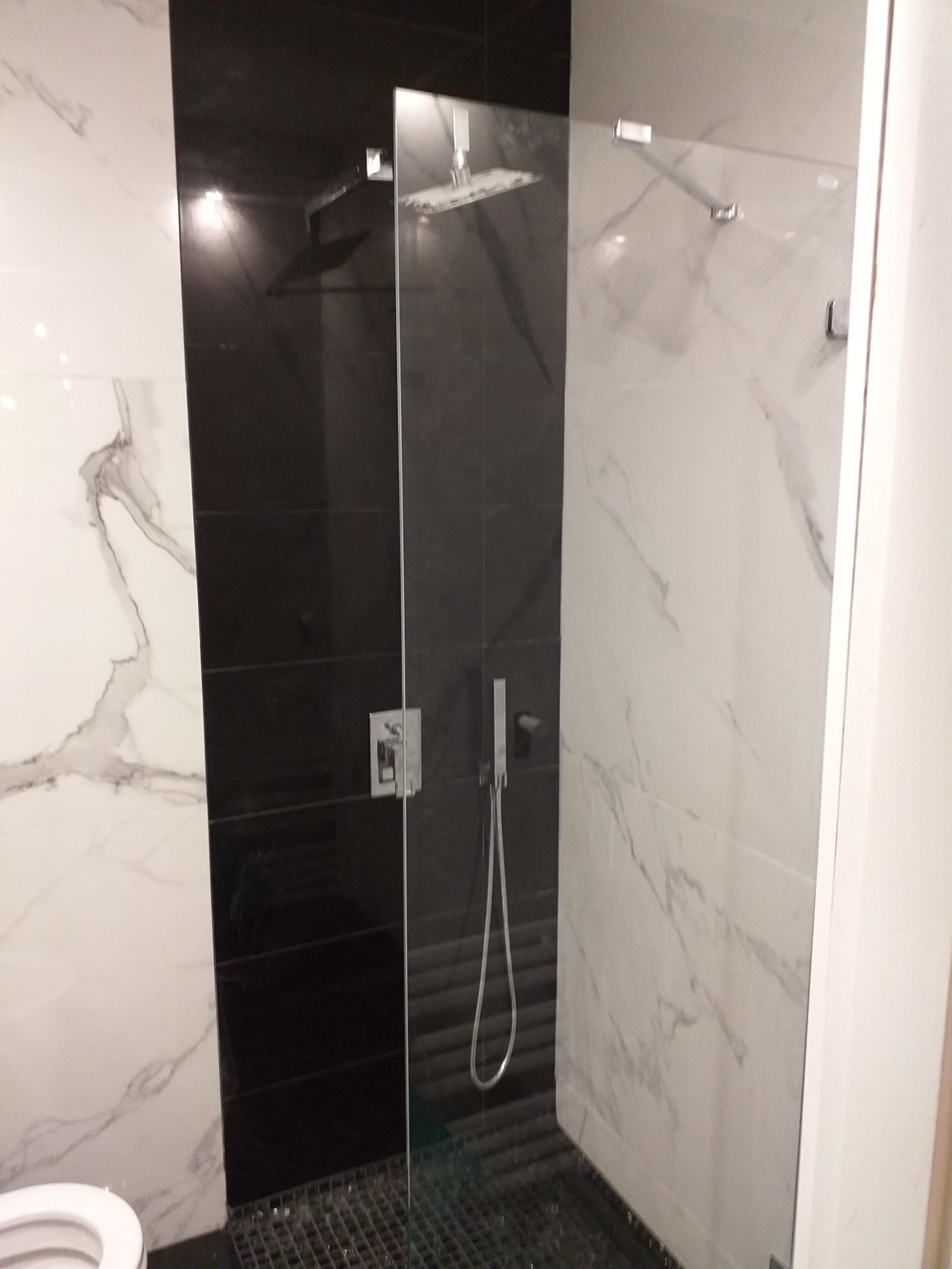 Nowoczesna kabina prysznicowa walk-in z czarnymi i białymi płytkami imitującymi marmur, wyposażona w deszczownicę i baterię podtynkową.