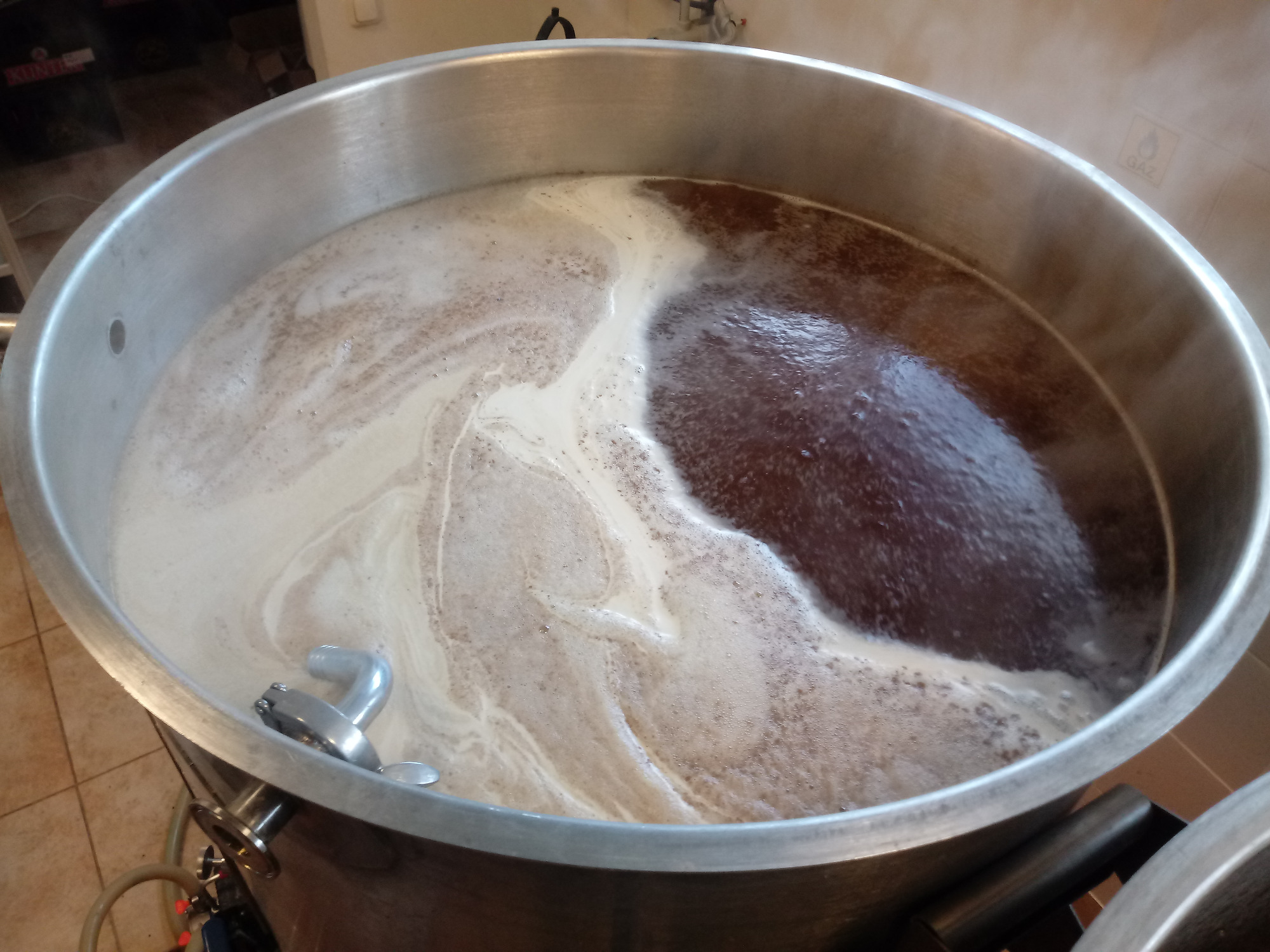 Zacieranie słodu w dużym, stalowym kotle z widoczną pianą i parą, proces warzenia piwa.