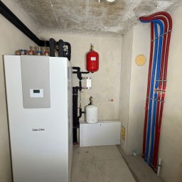 MONTEAM PIOTR POLAK - Biała pompa ciepła Stiebel Eltron w pomieszczeniu technicznym. Instalacja hydrauliczna z rurami w kolorze czerwonym i niebieskim. Stara Kamienica.
