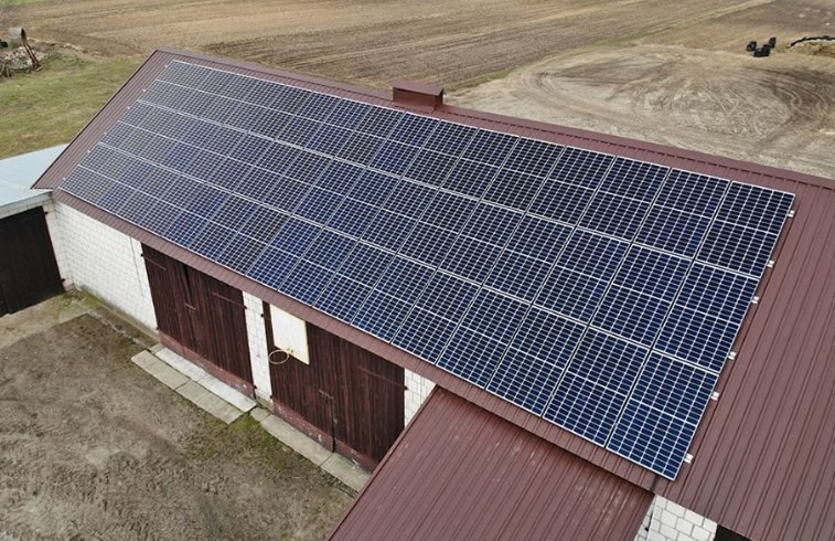 Panele fotowoltaiczne zamontowane na dachu budynku gospodarczego z cegły i brązowej blachy, widok z góry.