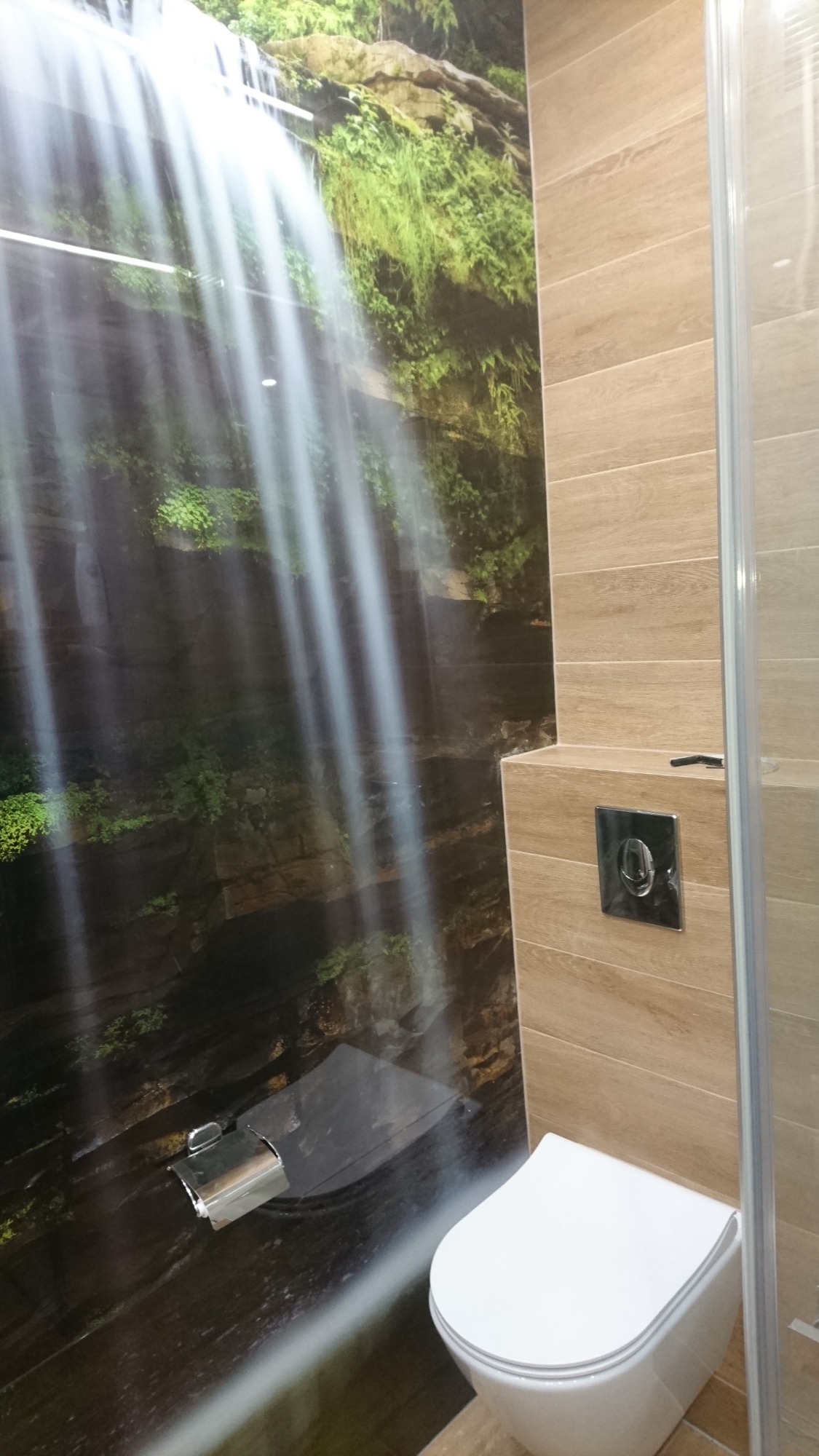 Nowoczesna łazienka z toaletą wiszącą i fototapetą imitującą wodospad na ścianie.