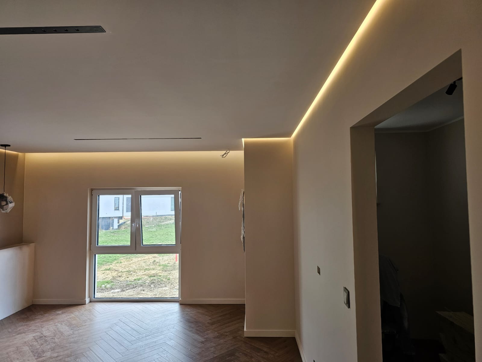 Jasne wnętrze z parkietem ułożonym w jodełkę, oświetleniem LED w suficie i oknem z widokiem na zewnątrz.