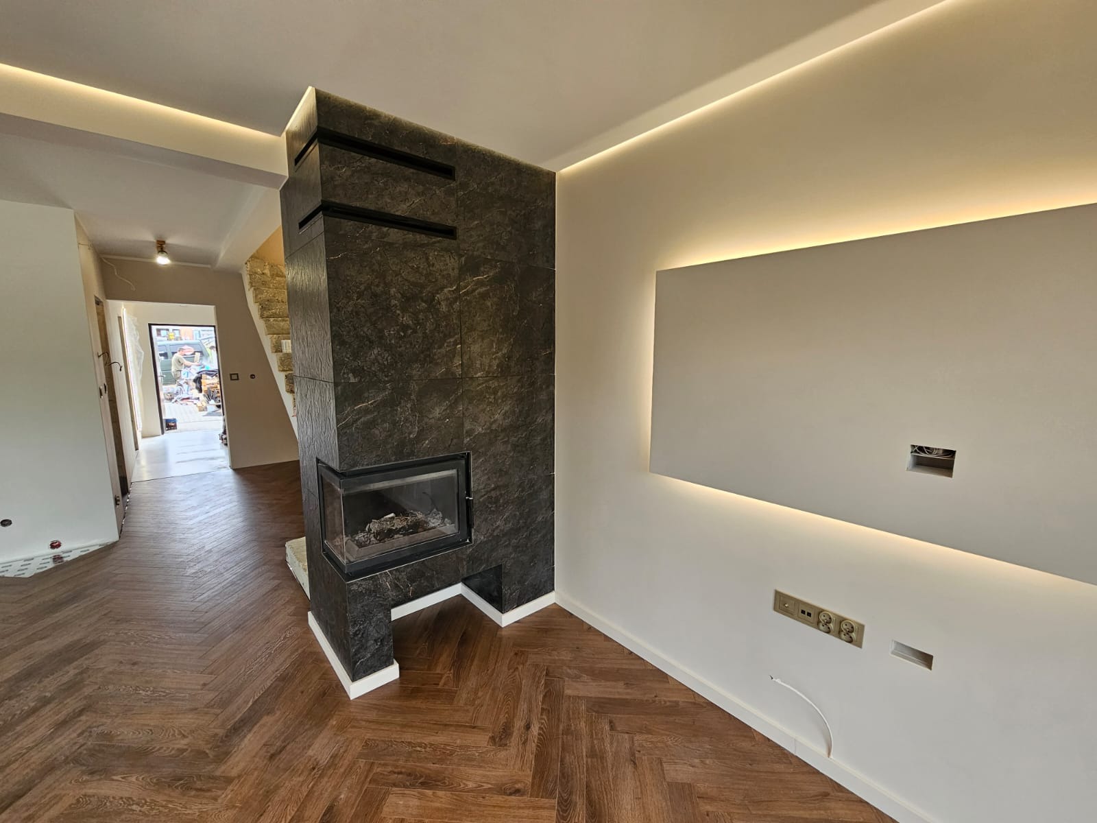 Nowoczesny salon z kominkiem obłożonym ciemnym kamieniem, parkiet ułożony w jodełkę, oświetlenie LED w suficie.