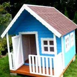 Niebieska, drewniana budka dla dzieci z brązowym dachem, białymi ramami okiennymi i balustradą, stojąca na trawniku.
