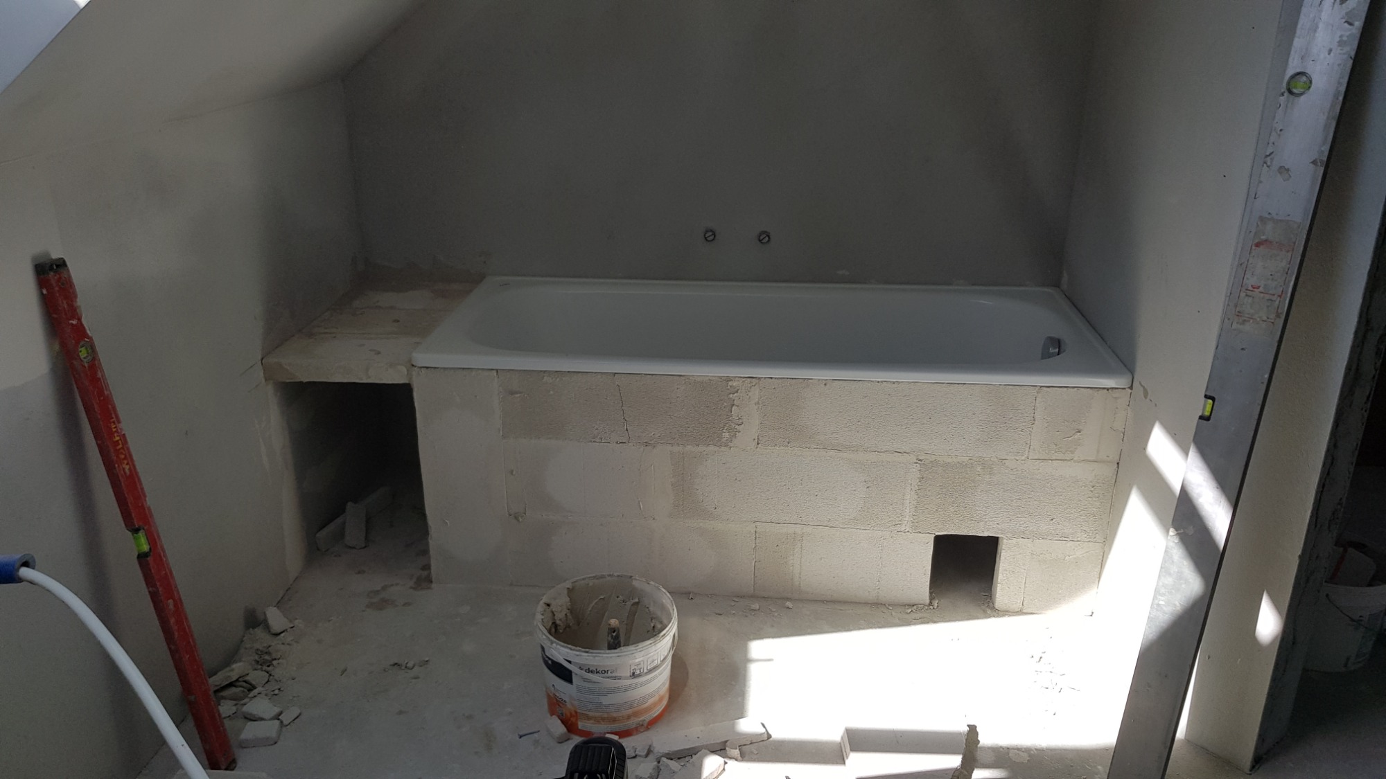 Wanna obudowana bloczkami z betonu komórkowego w trakcie prac wykończeniowych w łazience na poddaszu, widoczny poziomica, wiadro z zaprawą oraz gruz na podłodze.