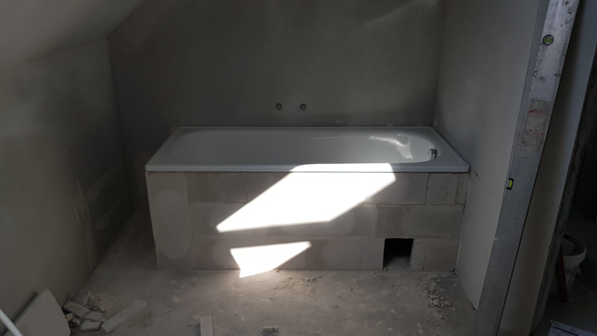 Wanna obudowana bloczkami w surowej łazience w trakcie prac, widoczne dwa punkty mocowania baterii na ścianie i fragment drabiny malarskiej z boku.