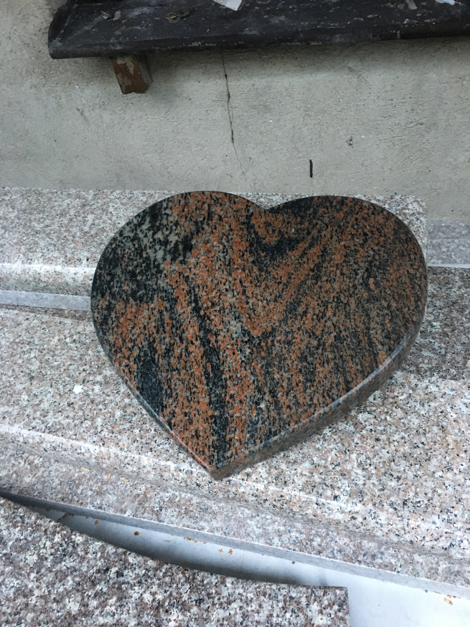 Serce z granitu w odcieniach brązu i czerni, leżące na blacie z jasnego kamienia. Obróbka kamieniarska, detal nagrobka.