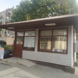 Fasada zakładu ślusarskiego z szyldem informującym o usługach, takich jak dorabianie kluczy i naprawa zamków, z reklamą 'Art-Key' na chodniku przed budynkiem.