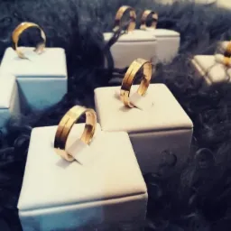 Zestaw złotych obrączek ślubnych z delikatnym rowkiem pośrodku, prezentowanych na białych, kwadratowych podstawkach na tle ciemnego, futrzanego materiału.