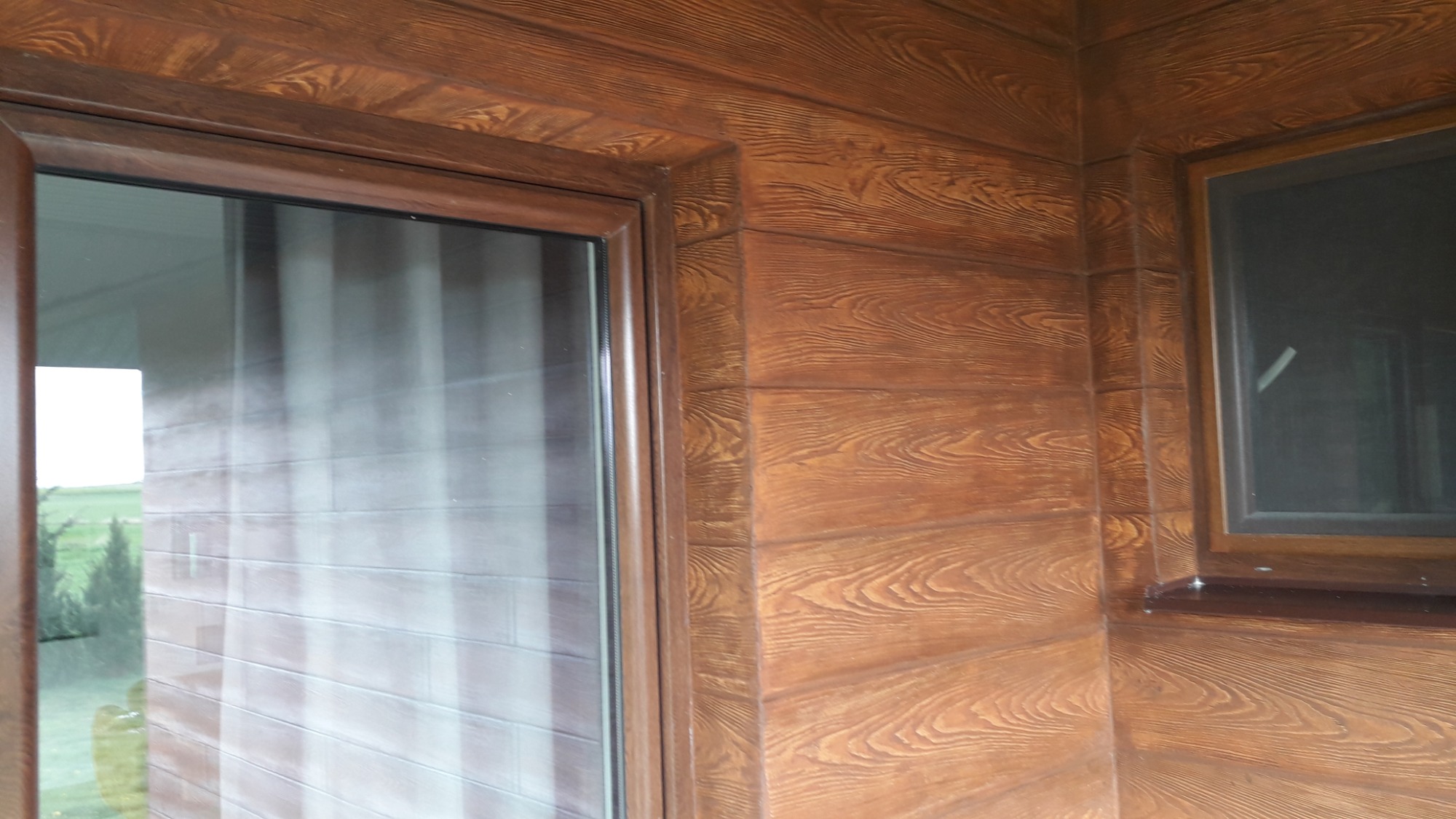 Elewacja budynku z drewnopodobnych paneli z widocznym oknem i narożnikiem, imitacja naturalnego drewna z wyraźnym usłojeniem.