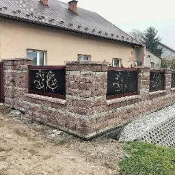 Nowoczesne ogrodzenie z cegły klinkierowej z czarnymi panelami dekoracyjnymi z motywem drzew, zabezpieczenie skarpy z ażurowych płyt betonowych.