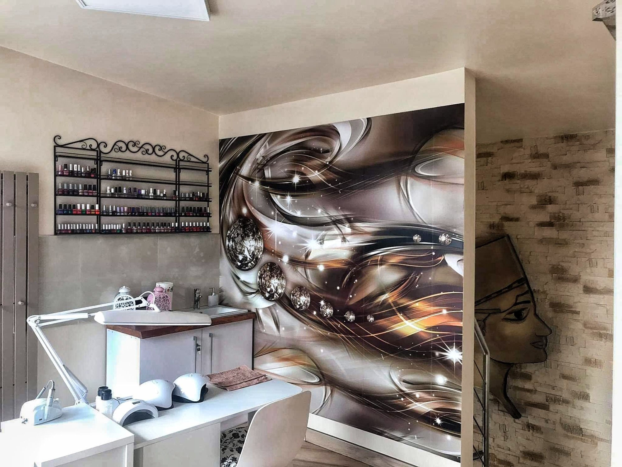 Wnętrze gabinetu kosmetycznego z dekoracyjną tapetą w abstrakcyjne wzory, półką na lakiery do paznokci i stanowiskiem do manicure z lampami UV.