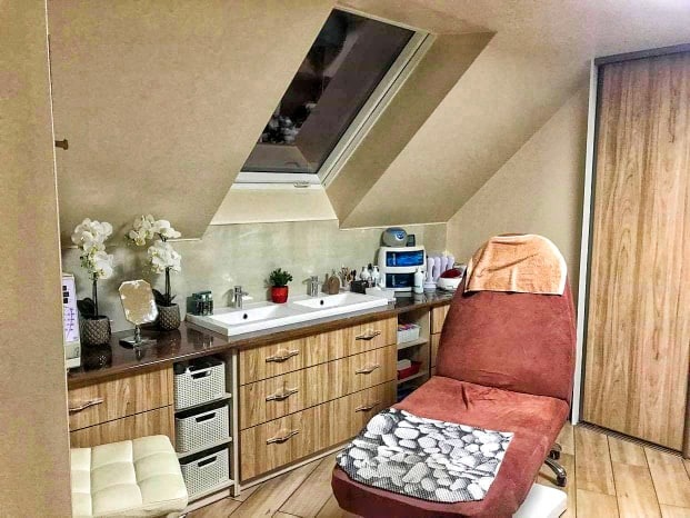 Wnętrze łazienki na poddaszu w Brzesku z oknem dachowym, wyposażone w podwójną umywalkę z szafką w drewnianym dekorze, fotel kosmetyczny i dekoracje roślinne.