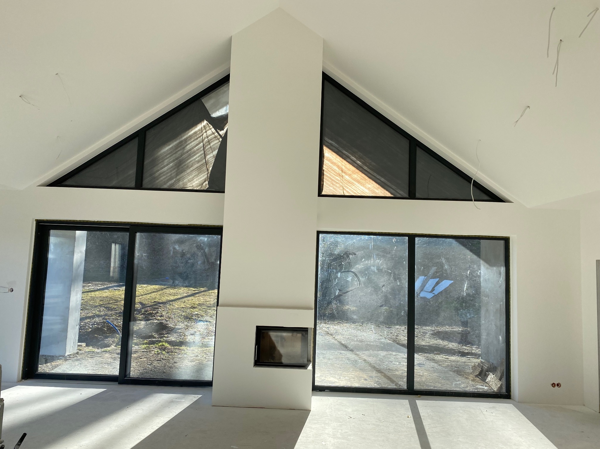 Wnętrze po remoncie w Lubinie: białe ściany, duże okna z czarnymi ramami i kominek. Widoczne niedociągnięcia wykończeniowe.