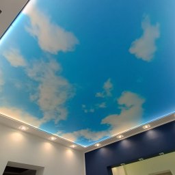 BUDiREM Darek Polaczek - Niebieski sufit napinany z motywem chmur, oświetlenie LED wzdłuż krawędzi, widoczny fragment drabiny malarskiej w rogu pomieszczenia.