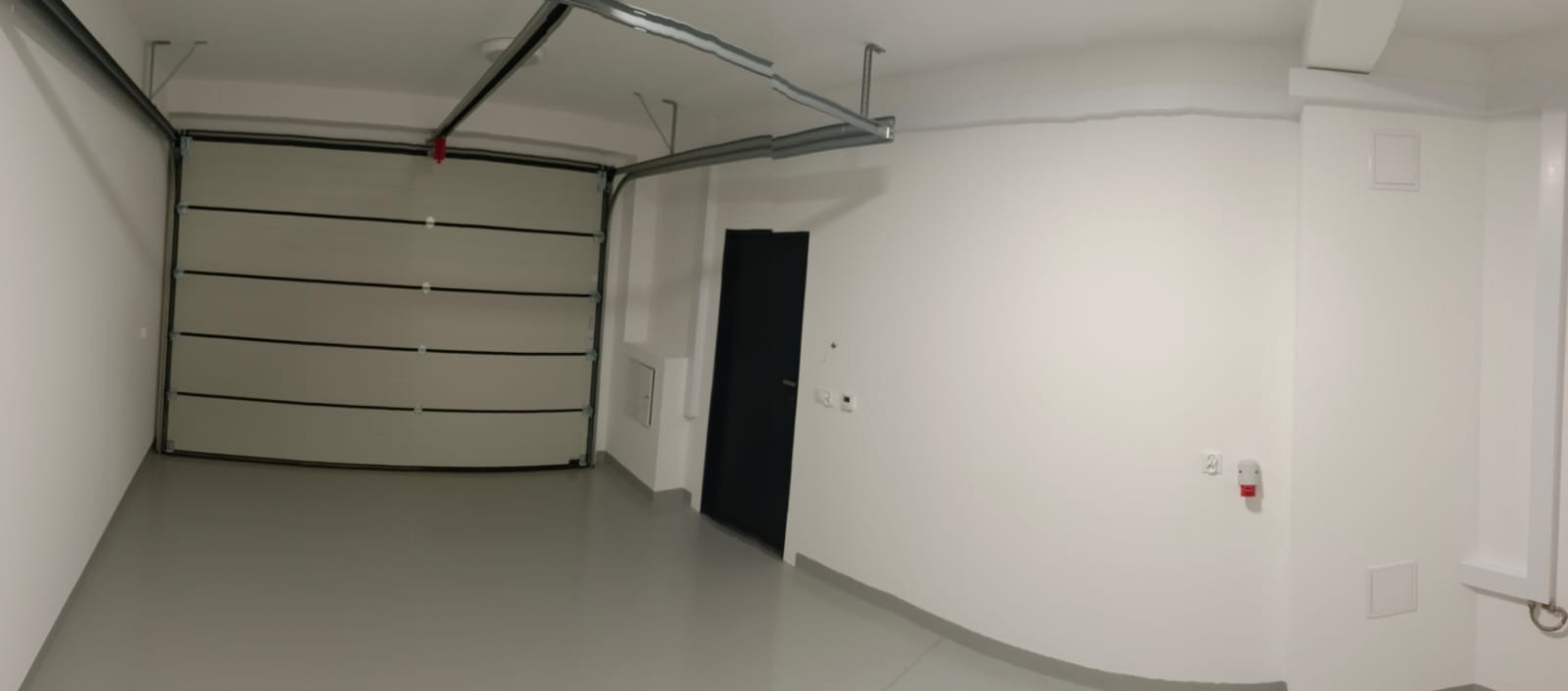 Wnętrze garażu z segmentową bramą garażową, szarą posadzką żywiczną i białymi ścianami po remoncie.