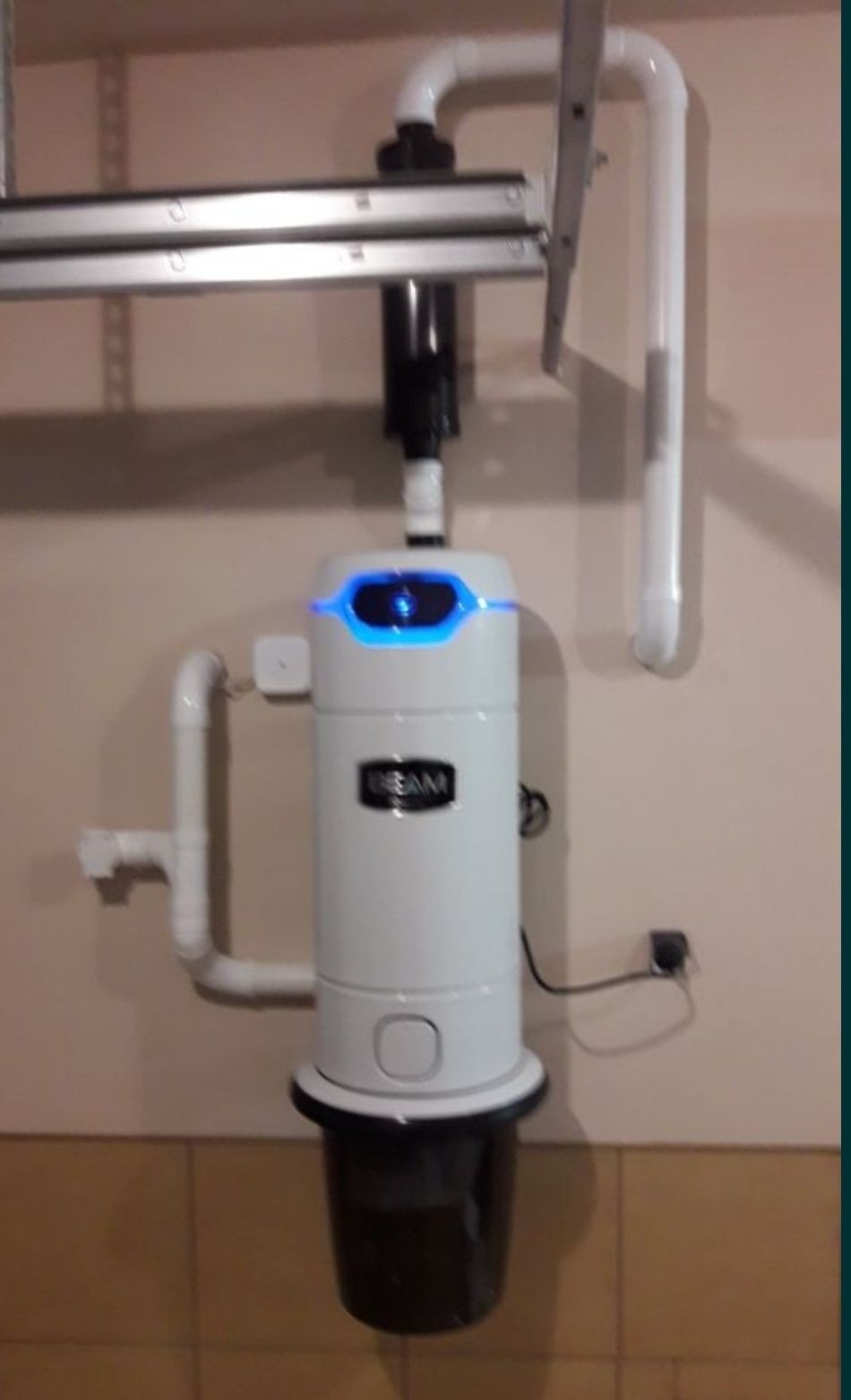 Centralny odkurzacz BEAM zamontowany na ścianie, z widocznymi rurami instalacji oraz podświetleniem LED.