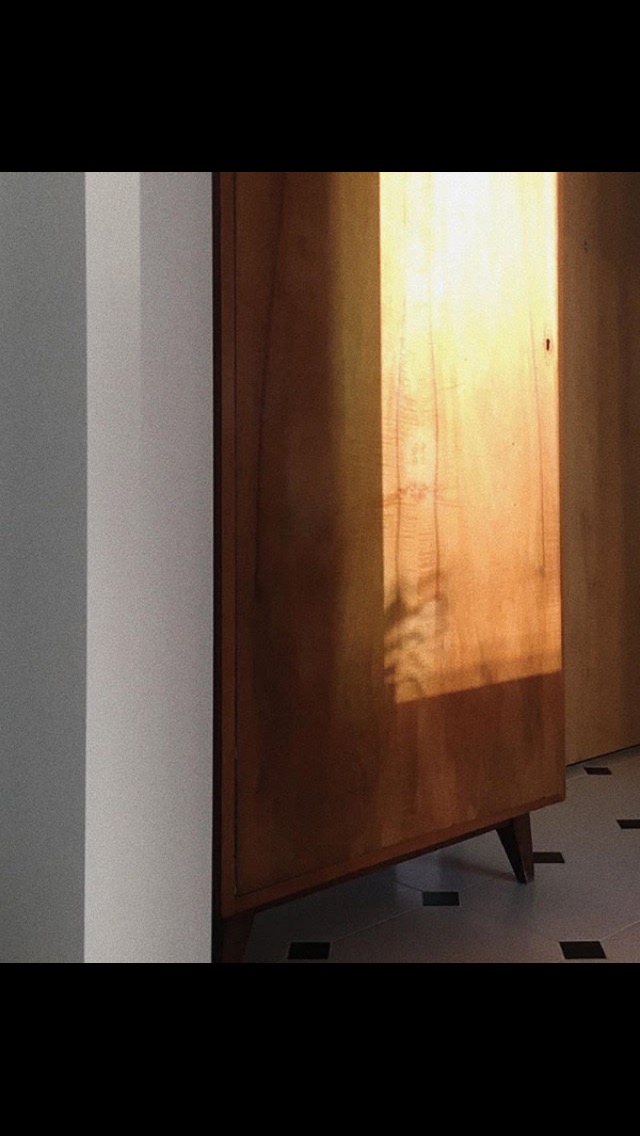 Drewniana szafka łazienkowa w stylu vintage oświetlona popołudniowym słońcem, z widocznymi płytkami podłogowymi w czarno-białą szachownicę.