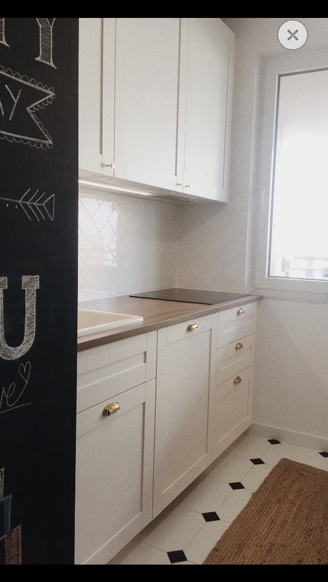 Jasna kuchnia z białymi szafkami, złotymi uchwytami i czarną tablicą z rysunkami kredą po lewej stronie