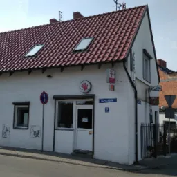 Budynek usługowy z szyldami T-Mobile i lokalnego serwisu komputerowego na rogu ulicy Piaskowej.