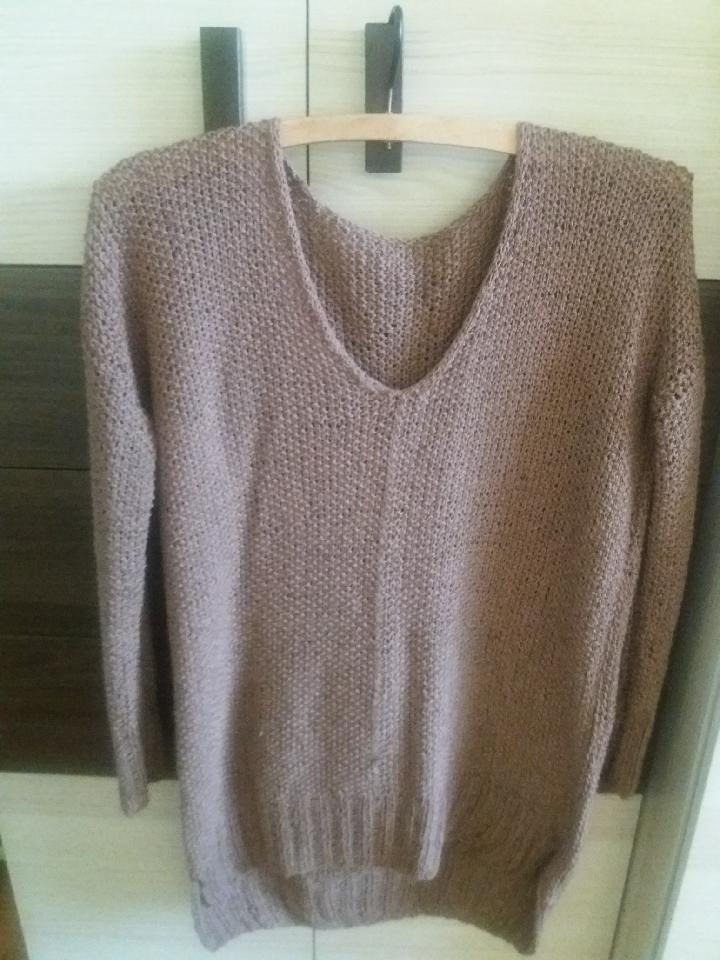 Brązowy, ręcznie robiony sweter z dekoltem w serek, wiszący na drewnianym wieszaku na tle szafy z ciemnymi uchwytami.